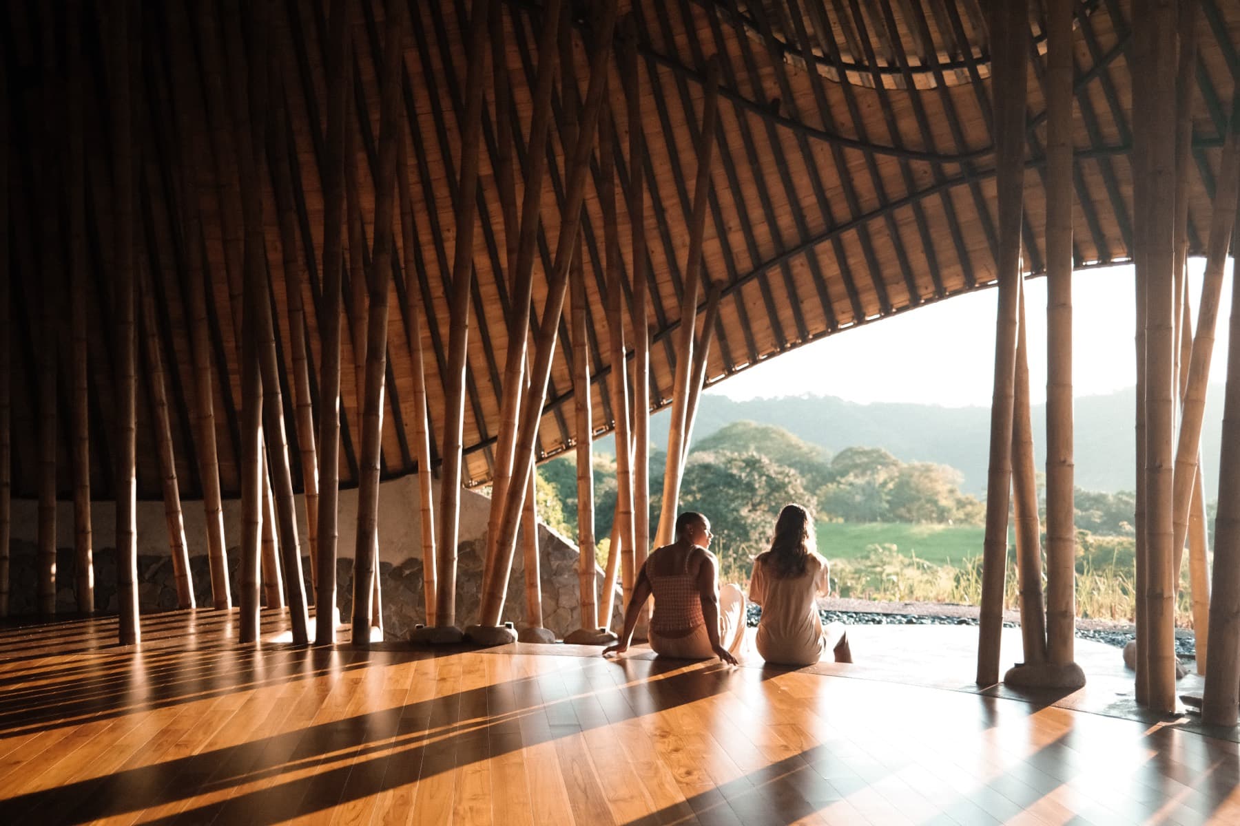 Two residents sitting on the ceremony space floor at golden hour, looking out at the hills