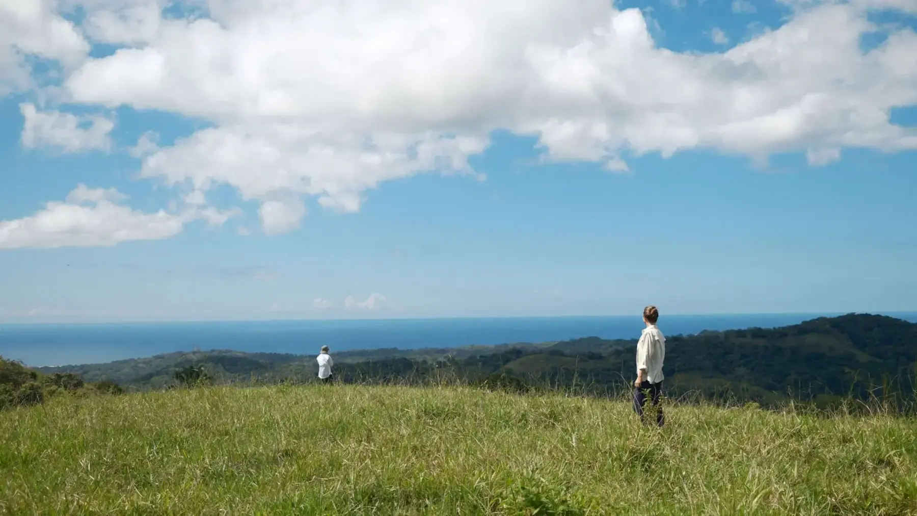 Two people walking the green hills above Nosara in the rainy season, the Pacific in the distance