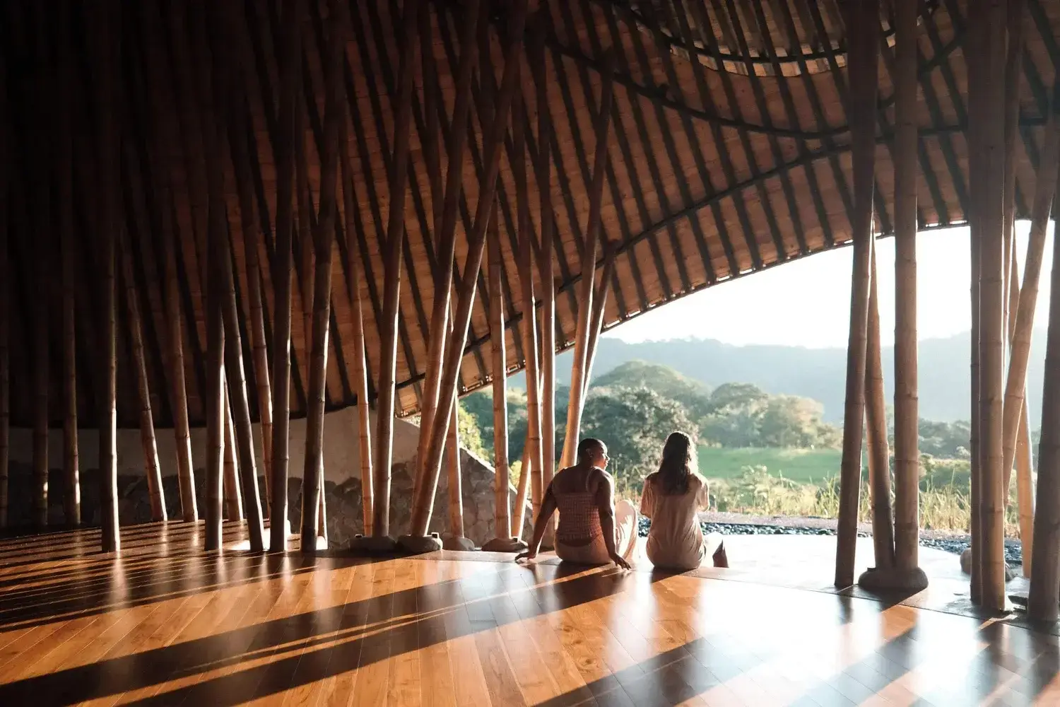 Two people sitting inside the Ibuku-designed bamboo maloca at Tierramor, looking out over the hills